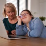 Down syndrome woman using computer with help of her mother